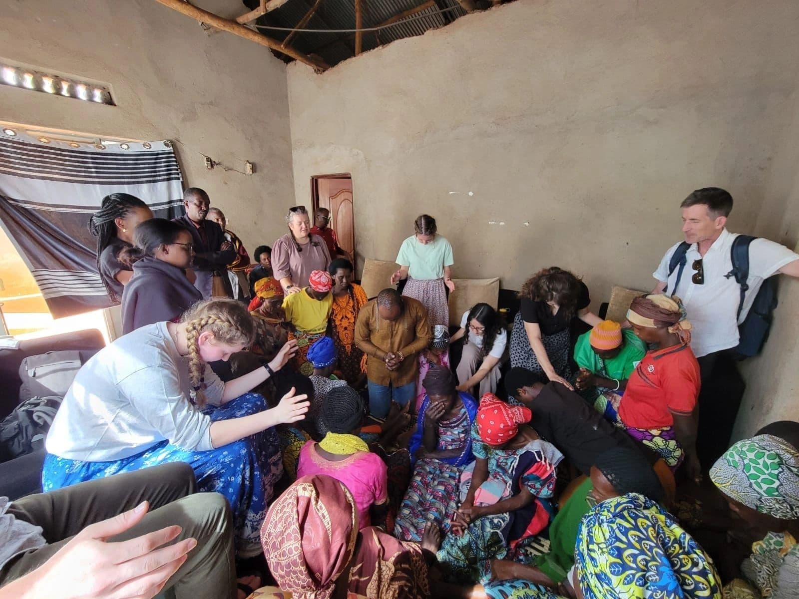 A room full of people seated closely together on the floor and on benches during a group counselling session, with facilitators kneeling among them.